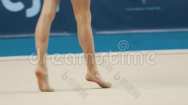 年轻女子在<strong>艺术体操</strong>比赛中的腿-穿着泳装的女孩在舞台上行走并滚动球